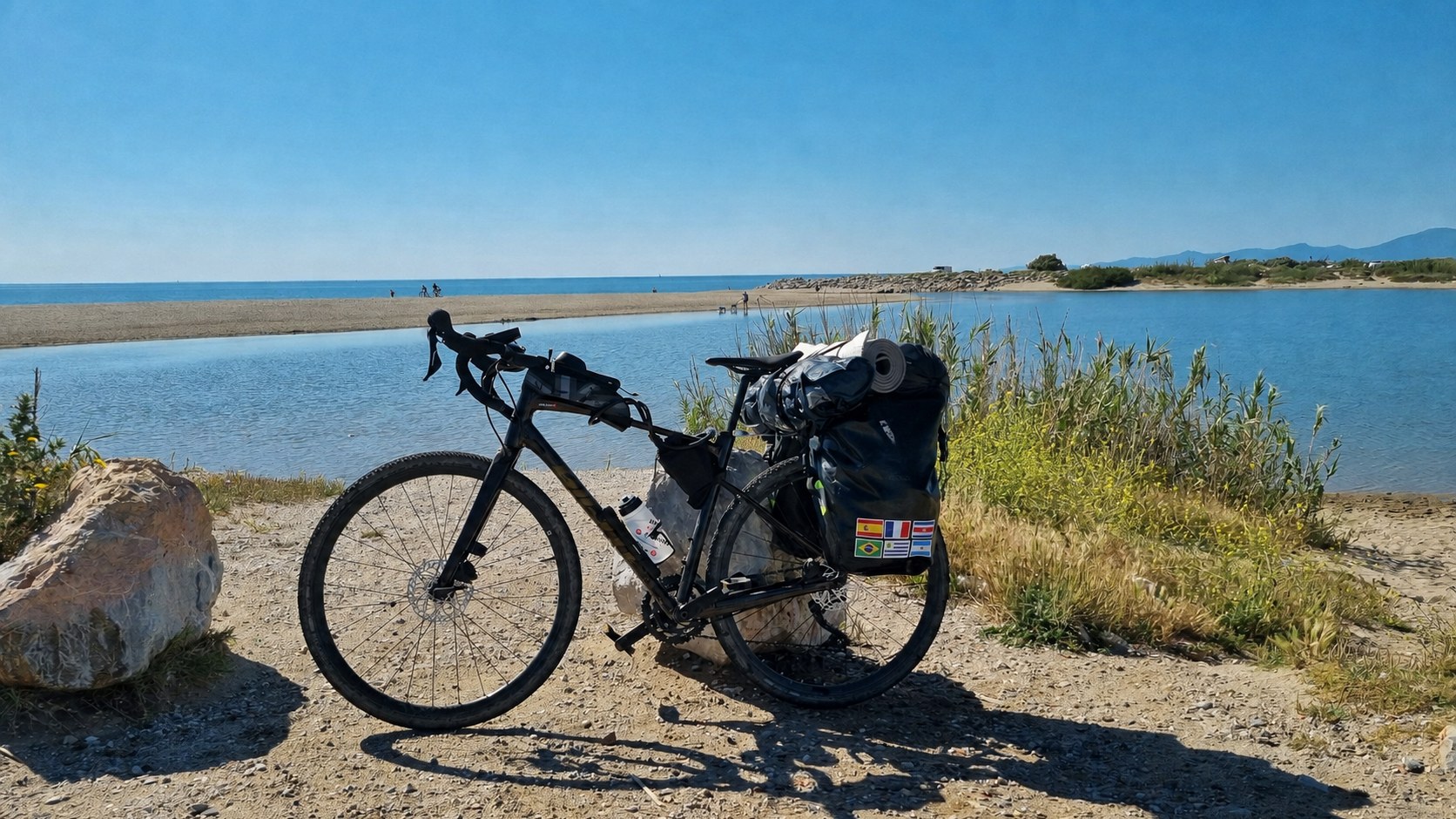 Bicicleta de bikepacking cargada, con alforjas y colchoneta, junto a una playa